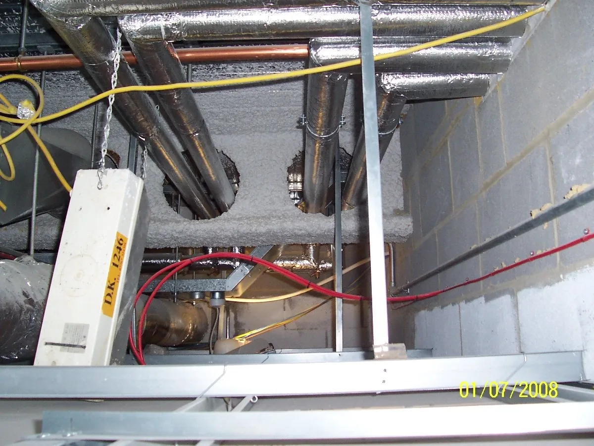 A ceiling with a bulkhead light chained to it, a loose fire alarm cable and a foam-covered beam