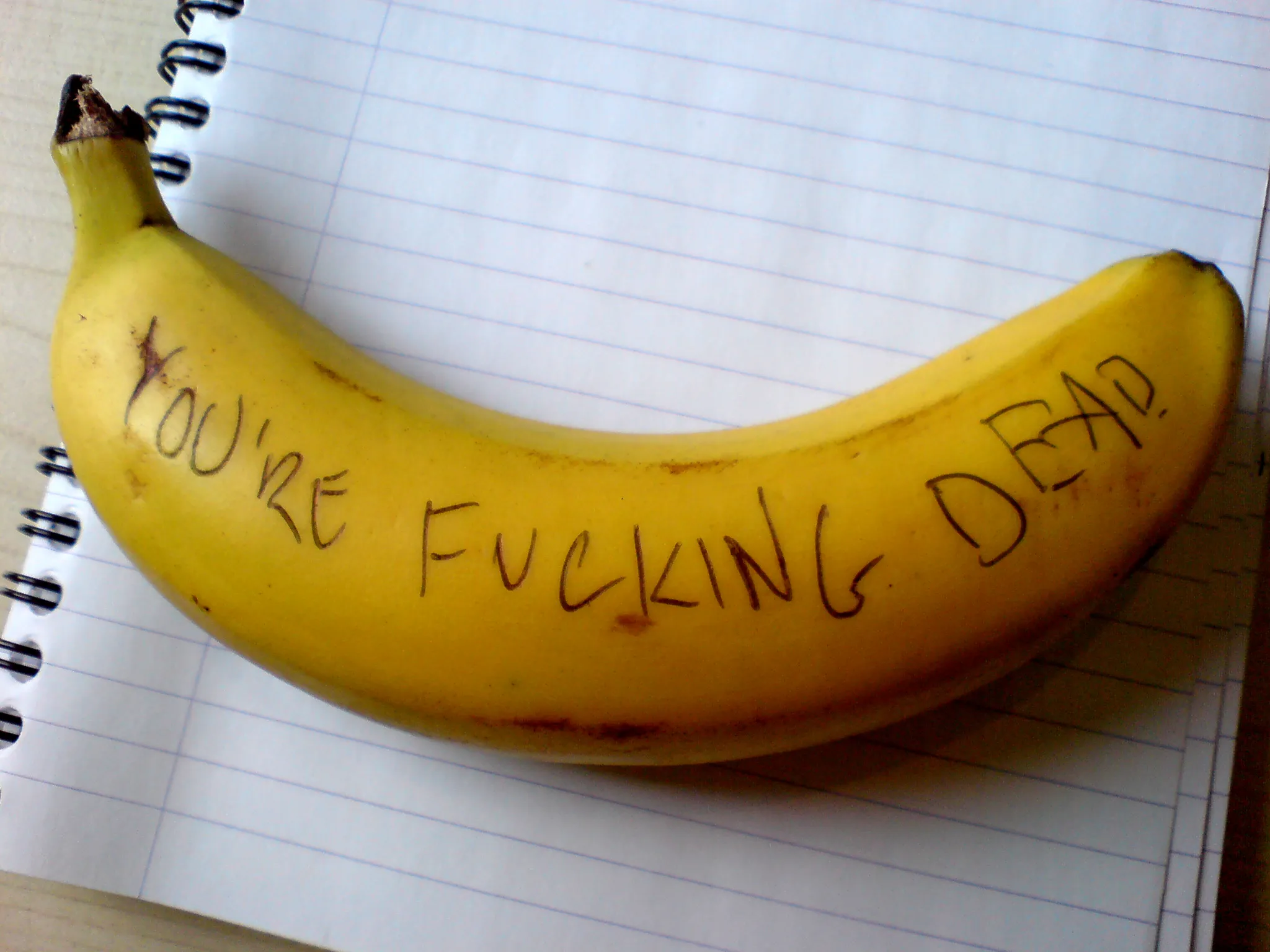 Photo of a banana with the words “You’re fucking dead” written on it