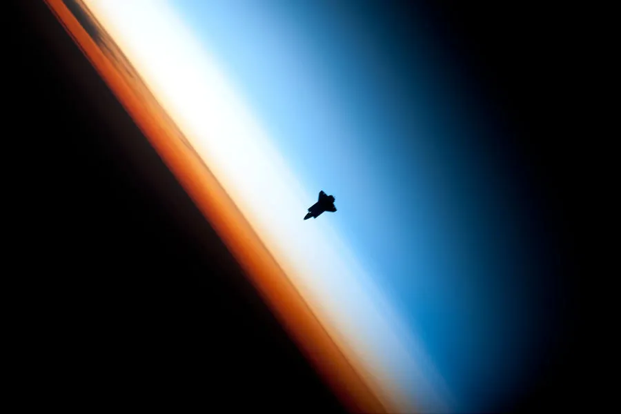 Space Shuttle Endeavour silhouetted against the bands of Earth’s atmosphere